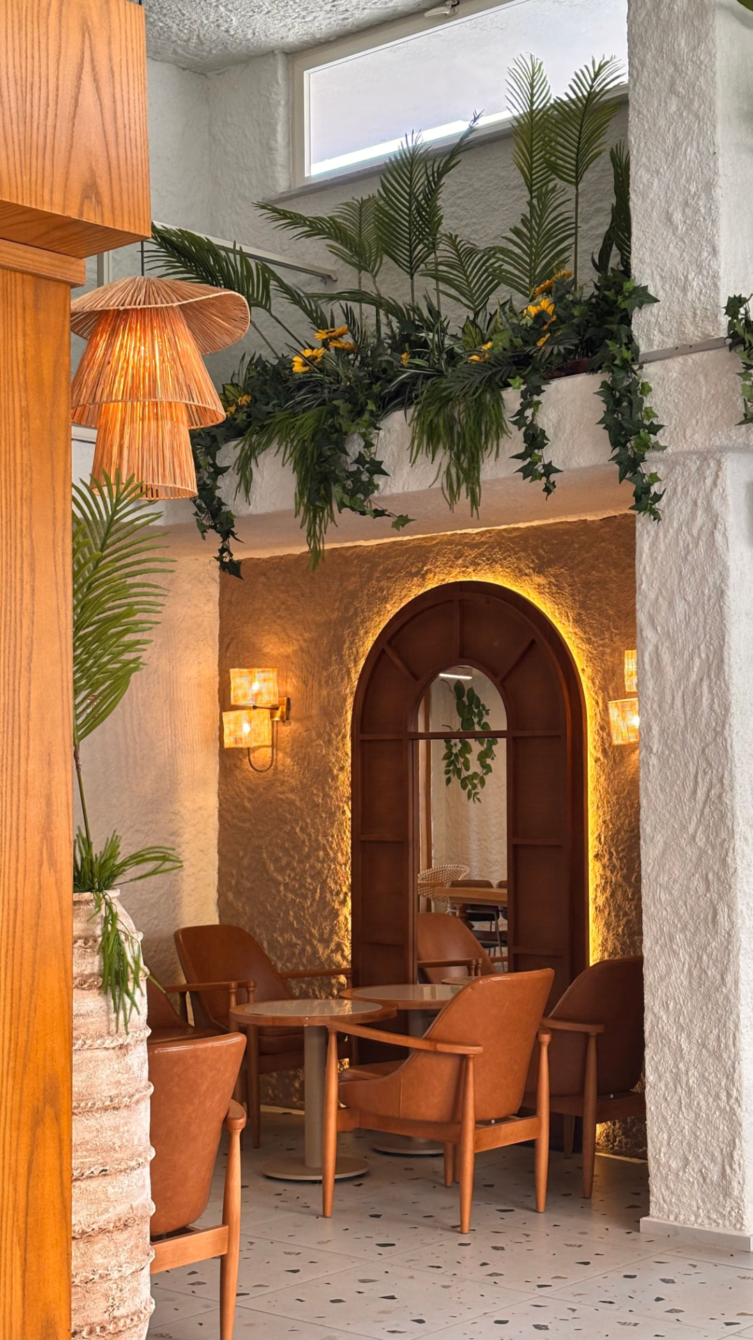 Caféhoek met cognacleeren fauteuils, een ronde houten boogspiegel en hanglampen van riet